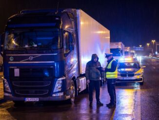 Nocna kontrola drogowa na autostradzie: obok oznakowanego auta inspekcji transportu funkcjonariusz w odblaskowej kamizelce sprawdza dokumenty kierowcy ciężarówki, w tle jadą kolejne tiry z włączonymi światłami, co nawiązuje do zasad kabotażu w UE i ryzyka wysokich kar przy nieprawidłowych zleceniach.
