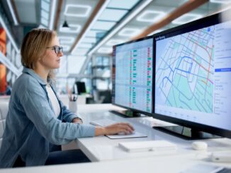 Specjalistka analizuje mapę tras i dane logistyczne na dużym monitorze w biurze – planowanie transportu i optymalizacja kosztów.