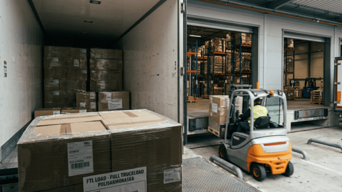 Wózek widłowy rozładowuje towar przy rampie magazynowej