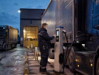 Elektryczny ciągnik siodłowy podłączony do ładowarki dużej mocy na placu bazy transportowej o zmierzchu.